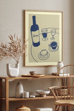 a table with plates, cups and vases on it in front of a framed wine bottle