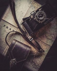 an old camera sitting on top of a map next to a leather bag and wallet