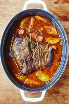 a pot filled with meat and vegetables on top of a wooden table