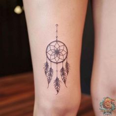 a woman's leg with a small dream catcher tattoo on the side of her thigh