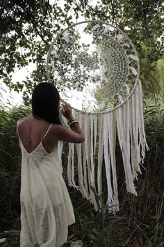 a woman standing in front of a tree holding a white dream catcher