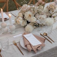 the table is set with white flowers and gold cutlery, napkins and candles