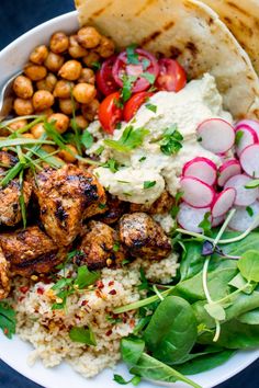 a white bowl filled with meat, rice and veggies next to pita bread