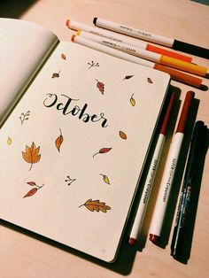 an open notebook sitting on top of a wooden table next to markers and pencils