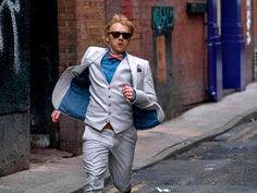 a man in a suit and bow tie is walking down the street while wearing sunglasses