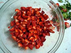 chopped strawberries in a glass bowl with parsley on the side and seasoning next to it