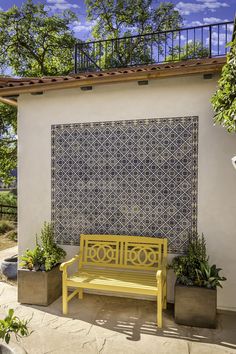 a yellow bench sitting in front of a white wall with blue and white tiles on it