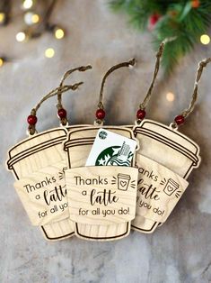 three wooden christmas tags hanging from a tree with holiday lights in the background, and one tag that says thanks to a latte for all you do