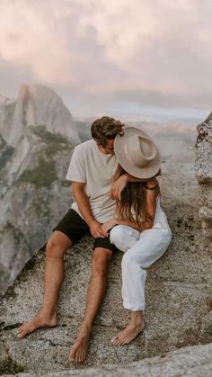 a man and woman sitting on top of a mountain hugging each other with mountains in the background