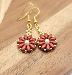 These red and gold earrings are very light weight, half an inch wide with a little over an inch drop. The flower shaped earrings are made of red glass twin beads, gold glass seed beads, with a pearl center. The earring wires are hook style. Hooks are gold, nickel-free and hypo-allergenic. Earring backs are made of clear silicone. Perfect for an event, holiday party, or paired with some cute jeans or leggings!  Please feel free to message me if you have any questions! Thank you for taking the tim Red Beaded Flower Shaped Jewelry, Festive Red Flower Earrings, Red Flower Beaded Earrings With Dangling Beads, Red Flower Earrings With Ear Wire For Party, Red Flower Earrings With Colorful Beads As Gift, Handmade Red Flower Earrings For Festive Occasions, Red Drop Flower Earrings For Festive Occasions, Festive Red Flower Drop Earrings, Red Beaded Dangle Flower Earrings