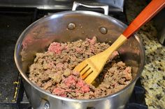 a wooden spoon in a pot filled with ground beef and meat sauce on the stove