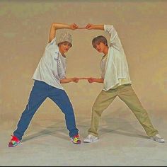 two young men standing next to each other in front of a beige background holding hands