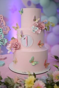 a three tiered pink cake with butterflies and flowers on the top, sitting on a table