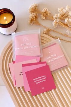 four pink cards sitting on top of a wooden tray next to a candle and some dried flowers