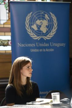 a woman sitting at a table in front of a blue sign with the logo of the united nations