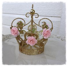 a gold glitter crown with pink roses on the front and sides, sitting on a table