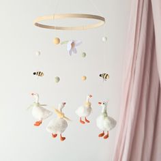 a baby mobile with ducks and bees hanging from it's sides in front of a pink curtain