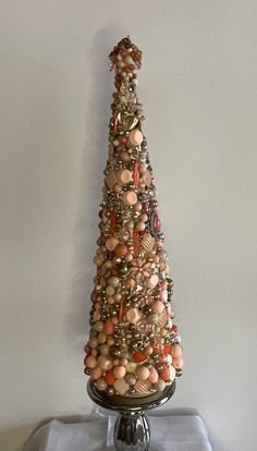 a christmas tree made out of seashells on a silver stand with a white wall in the background