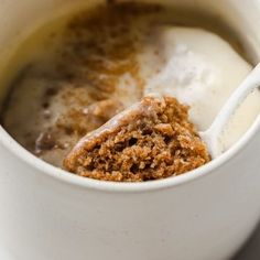 a spoon with some food inside of it in a cup next to a bowl full of milk