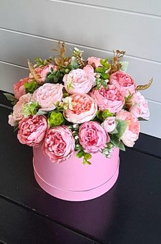 a pink hat box filled with flowers on top of a black table next to a white wall