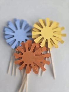 three paper flowers sitting on top of toothpicks in the shape of sunflowers