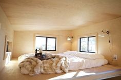 a bed with white sheets and blankets in a room next to two windows that look out onto the outdoors