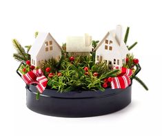 christmas decorations in a black container with white houses and red bows on the top, surrounded by greenery