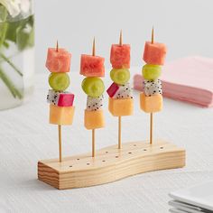 fruit skewers are arranged on wooden sticks in front of a vase with flowers