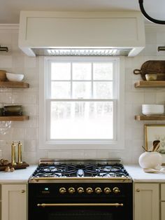 a stove top oven sitting inside of a kitchen next to a window with open shelves