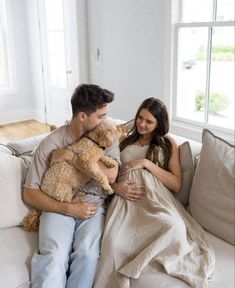 a man and woman sitting on a couch with a teddy bear in their arms while holding the baby