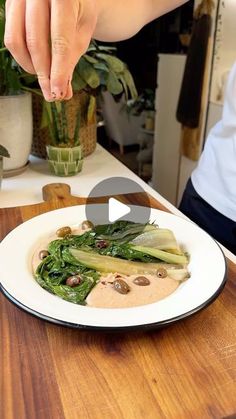 a person reaching for food on a plate with greens and mushrooms in the center, while another person holds out their hand