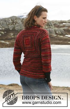 a woman standing in front of a body of water wearing a red and black sweater