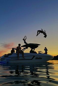 two people jumping off the back of a boat into the water at sunset with their arms in the air