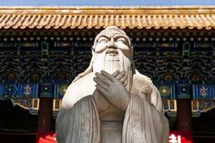 a statue of an old man with his hands together in front of a chinese building