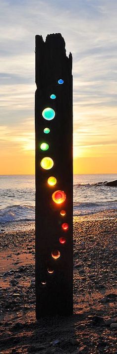 a piece of wood sitting on top of a sandy beach next to the ocean at sunset