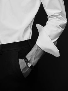 a man wearing a white shirt and black pants with his hands in his pockets,