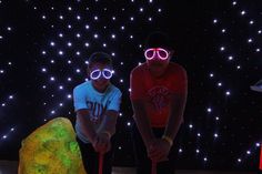 two young men wearing neon glasses standing next to each other in front of a rock