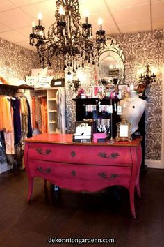 a pink dresser sitting inside of a room next to a chandelier and mirror