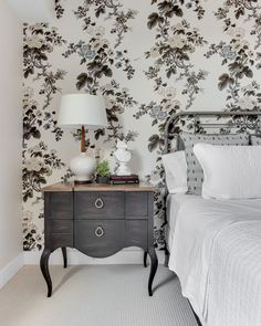 a bedroom with floral wallpaper and white bedding