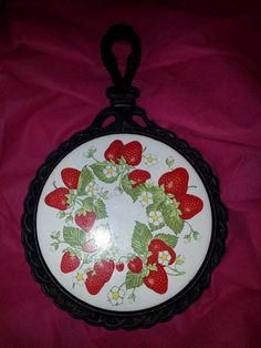 a white plate with strawberries and daisies painted on the front is hanging from a black metal hook