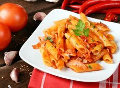 a white plate topped with pasta and sauce next to red peppers on a wooden table