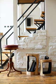 two wooden stools sitting on top of a hard wood floor next to a white brick wall