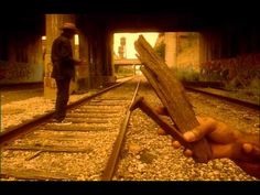 a person holding up a piece of wood in front of a man standing on train tracks