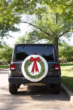 a black jeep with a wreath on it's back door is parked in front of a tree