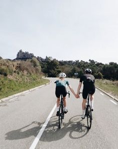 two bicyclists riding down the road holding hands