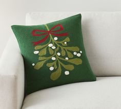 a green christmas pillow on a white couch with a red bow hanging from it's back