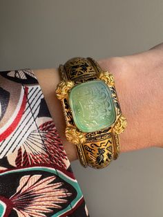 "This exquisite  archeological-revival bangle is attributed to Robert Phillips, circa 1865. The hinged bangle is decorated with Egyptian hieroglyphs in glossy black enamel culminating in a jade intaglio with a covered compartment to the reverse. \"ذات تو مظهر انعام سبحانی باد\", written in Farsi, it translates to, \"May your essence be a manifestation of divine blessings.\" A beautiful sentiment of well-wishing and hope for a positive and spiritually enriched existence. Hand fabricated in 15 karat gold, this bangle fits a petite 6\" wrist. A rare and wonderful jewel.    Weight: 28.1 grams Markings: none  Measurements: 6\" interior circumference, 1\" widest point (face) Notes: some losses to the enamel as shown" Traditional Jewelry With Historical Design For Collectors, Luxury Engraved Bracelets For Ceremonial Occasions, Luxury Handmade Ceremonial Bangle, Antique Intaglio Ceremonial Jewelry, Antique Intaglio Jewelry For Ceremonial Occasions, Antique Ceremonial Intaglio Jewelry, Ceremonial Antique Yellow Gold Cuff Bracelet, Luxury Ceremonial Bangle With Intricate Design, Traditional Ceremonial Intaglio Jewelry