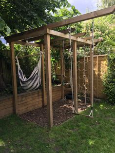 a hammock hanging from a wooden structure next to a fence and grass area