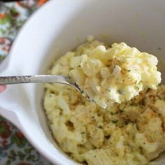 a person holding a spoon full of mashed potatoes in a white bowl with parsley sprinkled on top