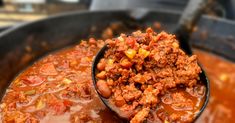 a ladle full of chili and ground beef in a large pot filled with broth